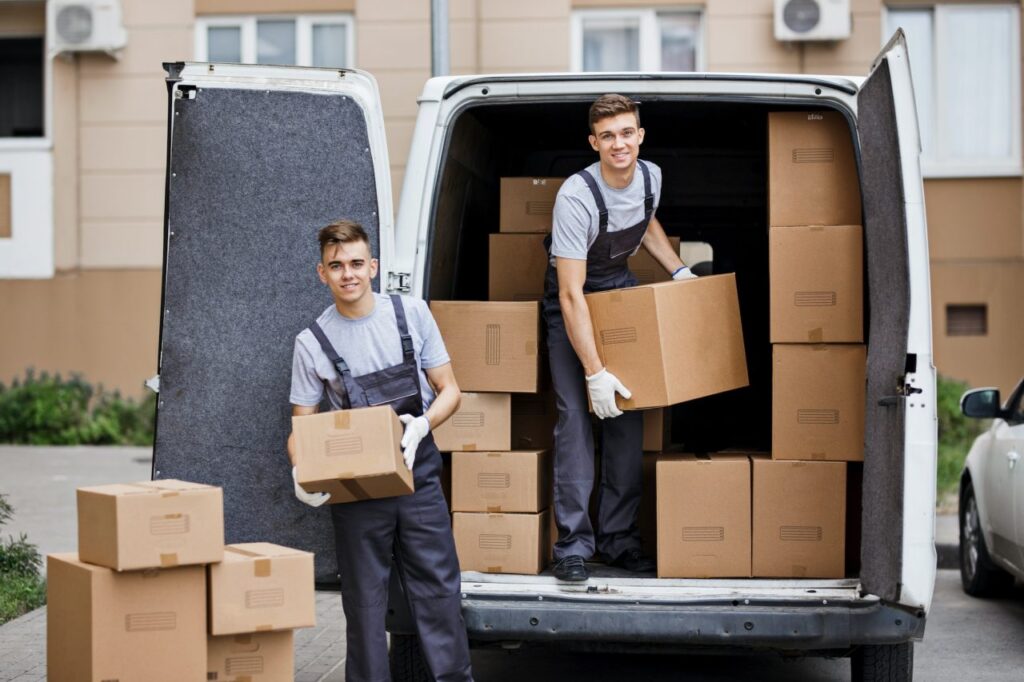 two young handsome smiling movers wearing uniforms are unloading the van full of boxes house move